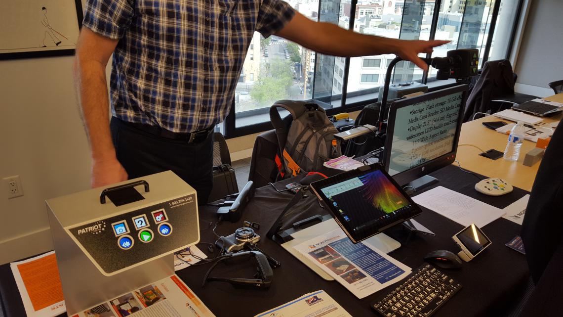 Table with device called the Patriot Voice Plus Reading Machine, eSight Glasses, Mobile Screen magnifier and a desktop Screen Magnifier