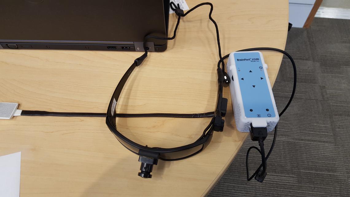 Table with BrainPort device which consists of a pair or sunglasses with a camera located in the middle of the frame with a cable going from the glasses to a control box that then connect to the output device that is placed on the tongue.